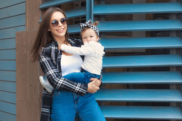 Happy mother and daughter have fun and wearing a jeans clothes in city. Street style family look.