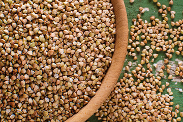 Buckwheat in a wooden bowl on an old green wooden table, closeup view