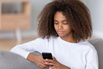 Close up african teenager girl sitting on couch using smartphone