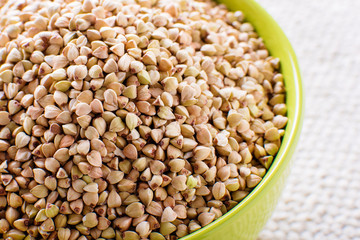 Wooden bowl with green buckwheat on white background. Close-up.