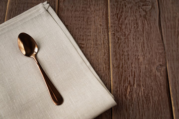 Top view of cloth napkin of beige color and served tea spoon on wooden table.