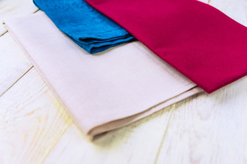 close up of cloth napkins of beige, blue and burgundy colors on rustic white wooden table.