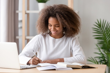 Positive african schoolgirl sitting at desk and study