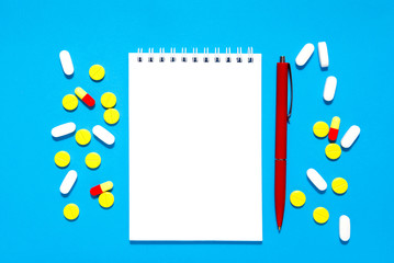 Notepad for notes, pen and tablets on a blue background.