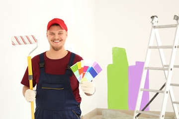 Male painter in uniform with roller brush and color palette samples indoors