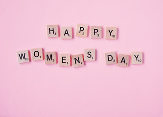 Top view Message happy woomans day spelled in wooden blocks on pink background. Love, 8 march background. Gift, greeting, compliment concept. Copy space. place for text