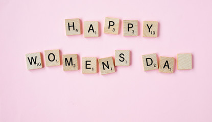 Top view Message happy woomans day spelled in wooden blocks on pink background. Love, 8 march background. Gift, greeting, compliment concept. Copy space. place for text