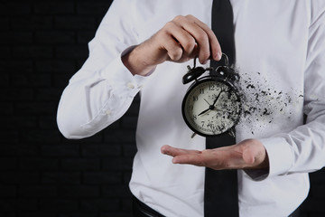 Businessman with alarm clock on dark background, closeup