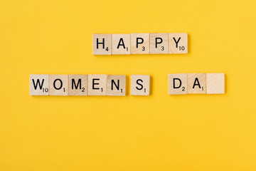 Top view Message happy woomans day spelled in wooden blocks on yellow background. Love, 8 march background. Gift, greeting, compliment concept. Copy space. place for text