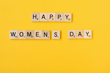 Top view Message happy woomans day spelled in wooden blocks on yellow background. Love, 8 march background. Gift, greeting, compliment concept. Copy space. place for text