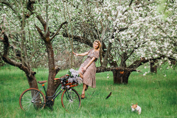 girl blonde in dress sits on a tree near the bike and beside the runner dog