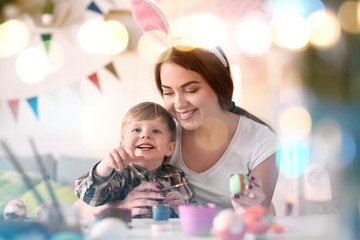 Mother painting Easter eggs with her child at table
