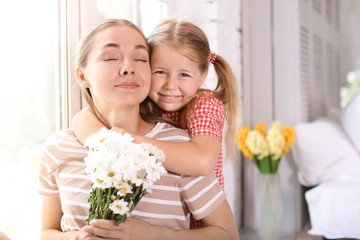 Portrait of cute little girl and her mother with flowers at home