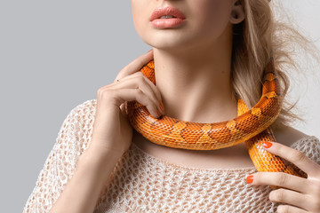 Young, beautiful, woman with snake around her neck on grey background. Double-cross, foul play, perfidy, betrayal, treachery concept. False friendship. Judas. Stab in the back.
