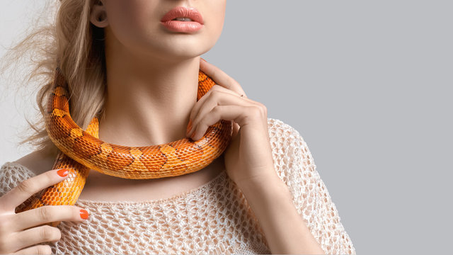 Young, beautiful, woman with snake around her neck on grey background. Double-cross, foul play, perfidy, betrayal, treachery concept. False friendship. Judas. Stab in the back.