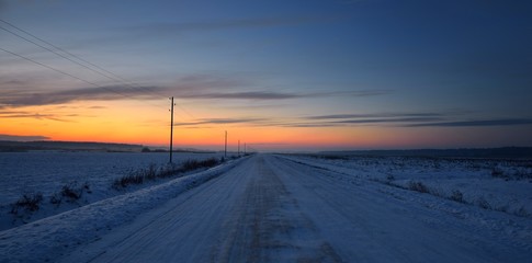Countryside road with telegraph poles on a winter day under snow at sunset