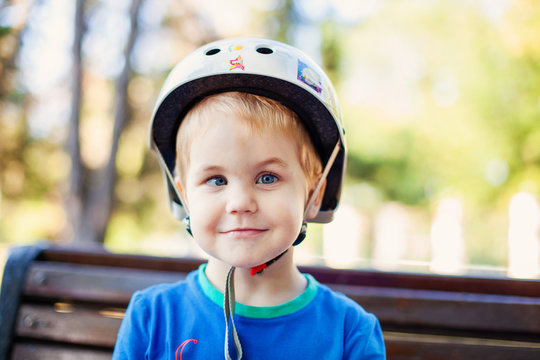 Little blonde boy 3 years old in white sport helmet and blue t-shirt outside. Special problems with kid's eyes. Myopie, astigmatism, cross-eyed