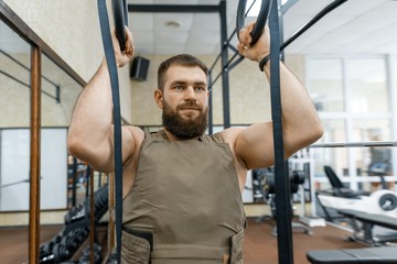 Military sport, muscular caucasian bearded adult man doing exercises in the gym dressed in a bulletproof armored vest