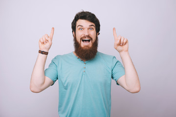 Fototapeta premium Portrait of young surprised handsome bearded man in casual tshirt pointing upside with both hands