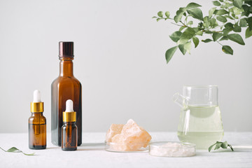 Obraz na płótnie Canvas Aromatherapy. Small glass bottles with cosmetic oils. Bath salt. Fresh leaf. Objects for spa procedures on white background oil, leaf.