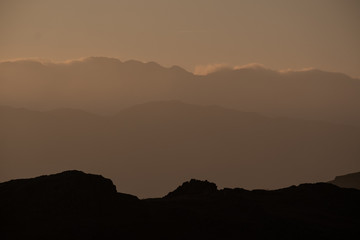 A silhouette of Crinkle Crags skyline created by evening light, seen from Loughrigg Fell, Lake District, UK