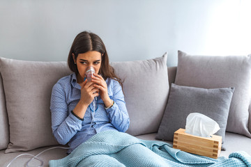 Use nebulizer and inhaler for the treatment. Young woman inhaling through inhaler mask lying on the...