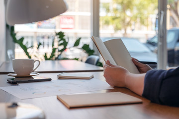 Closeup image of a woman holding and opening a blank notebook on wooden table