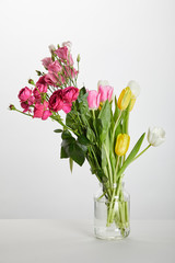fresh pink roses and yellow tulips in glass jar isolated on white
