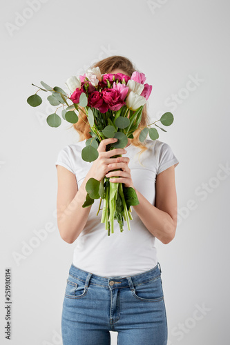 girl holding fresh bouquet with tulips, eucalyptus and roses in front of face isolated on grey