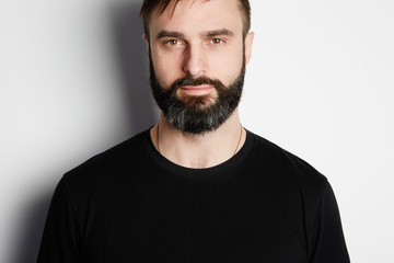 Obraz premium Portrait of bearded man in black tshirt on the empty background.
