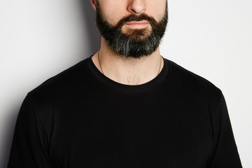 Portrait of bearded man in black tshirt on the empty background.