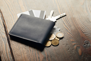 leather wallet, keys, cheque, coins and credit cards on wooden table