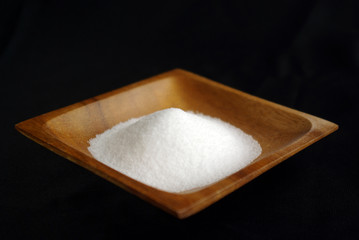 横長で黒い布背景にある正方形の木の器に盛られた白い塩