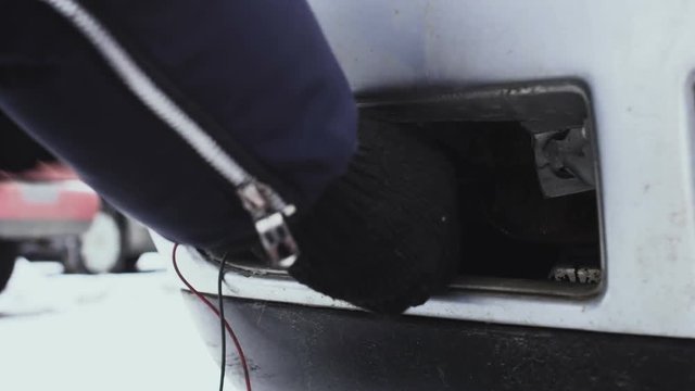 Man screwing towing loop into a car, close-up, winter