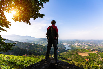 Man traveller stands on a cliff overlooking of river, the vineyards are on a hills Douro Valley,...