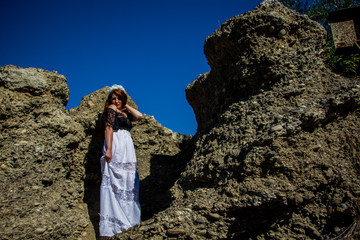 Portrait of young beautiful redhead woman in dress sitting on the rock and blue sky