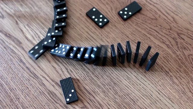 black domino cards with white dots in rows and balanced one after the other on a wooden table. Tiles of the domino before falling for a chain effect. Business disaster concept with domino effect