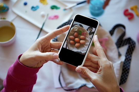 Happy easter preparing. Woman hands holding smartphone and making photo of colorful easter eggs on the table