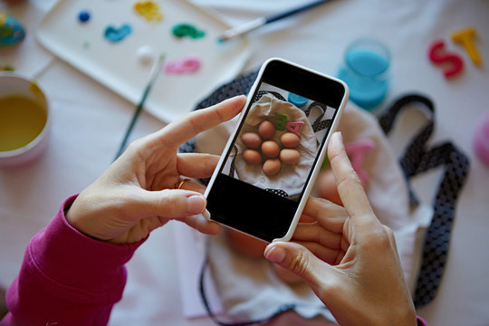 Happy easter preparing. Woman hands holding smartphone and making photo of colorful easter eggs on the table