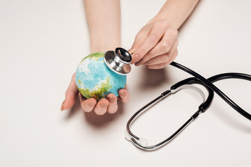 partial view of woman holding stethoscope and earth model on white background, global warming...