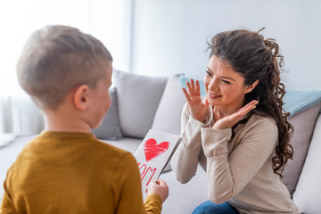 Mother receiving gift and greeting card from her cute little son at home