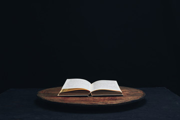 One open old book on a round wooden table. Beautiful dark background..