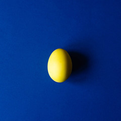 One easter egg of yellow color on a blue background. 