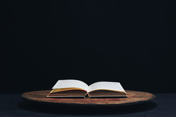One open old book on a round wooden table. Beautiful dark background..