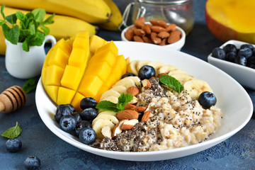 Good morning! Breakfast with oatmeal, banana, mango, blueberries and chia seeds on a concrete background.