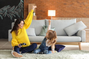 Pregnant mother with little daughter playing video games at home