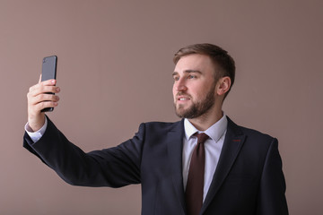 Handsome businessman taking selfie on color background