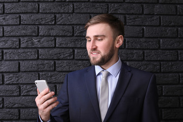 Portrait of handsome man with mobile phone on dark brick background