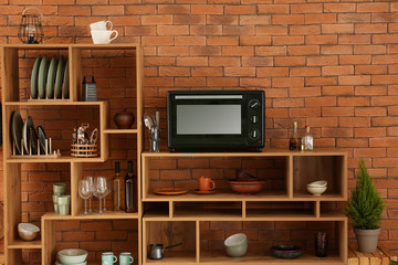Set of clean dishes with utensils and microwave oven on wooden shelves near brick wall