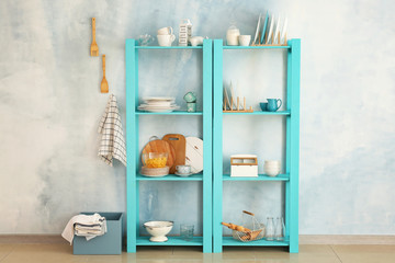 Set of clean dishes with utensils on shelves near light wall